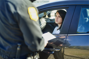 A police officer standing by a car window during a traffic stop with a female driver looking out.